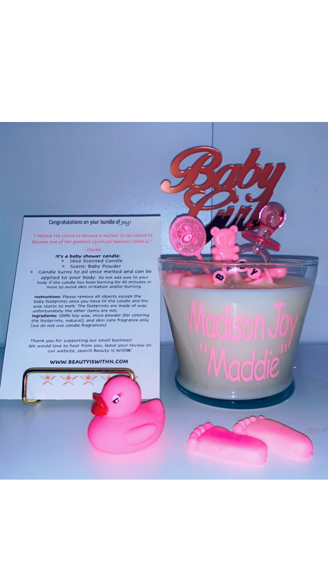 Pink 16oz baby shower candle with 'Baby Girl' topper, wax baby feet, rubber duck, and baby-themed decorations (decorations may vary on availability). Includes an instruction card and customizable label for baby's name. Scent: Baby Powder