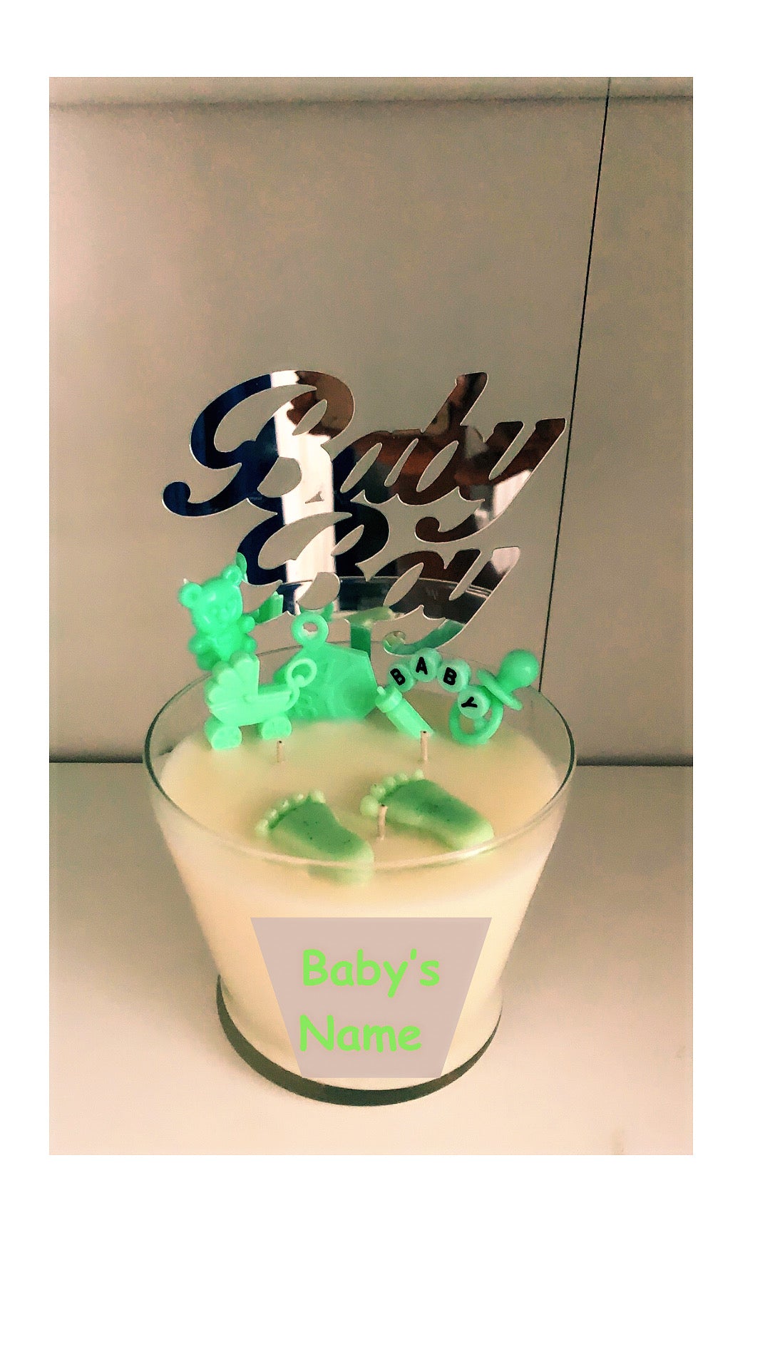 Green 16oz baby shower candle with 'Baby Girl or Boy' topper, wax baby feet, rubber duck, and baby-themed decorations (decorations may vary on availability). Includes an instruction card and customizable label for baby's name. Scent: Baby Powder